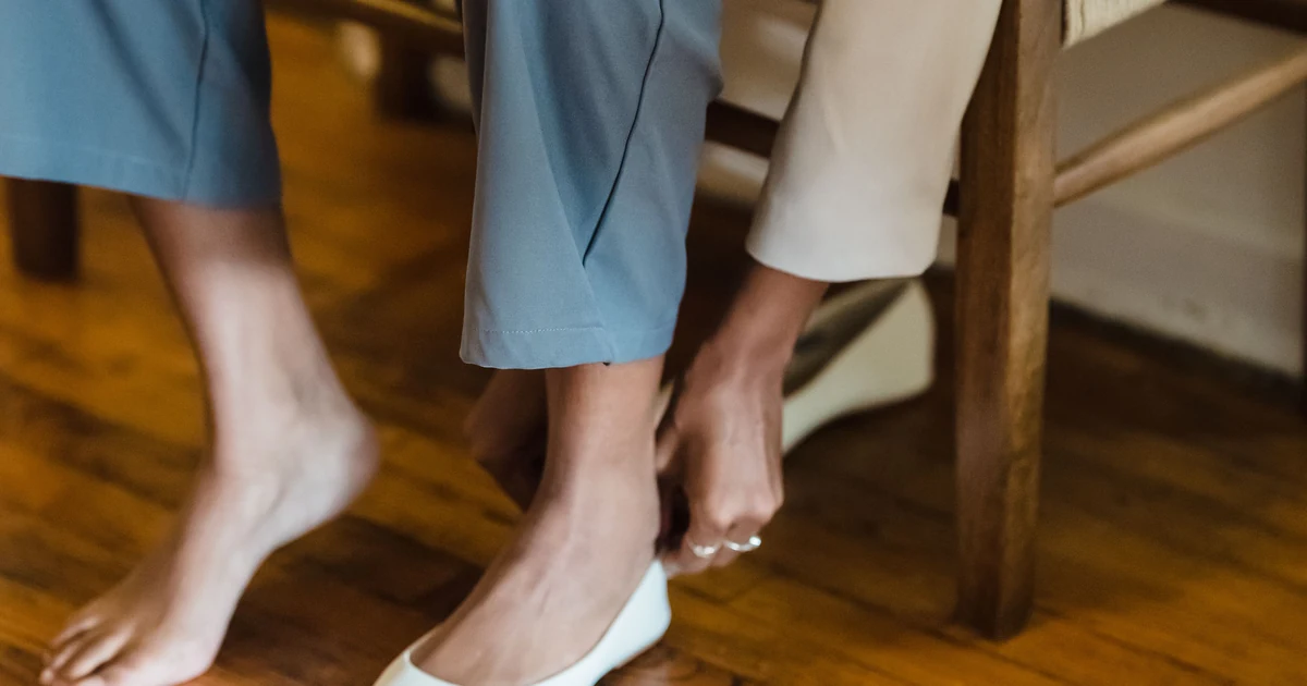 A woman puts on a white flat shoe while seated indoors.